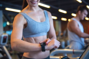 Çekici genç kadın onun etkinlik izleyicisi'ni seyir ve spor salonunda bir koşu bandı üzerinde çalıştırırken gülümseyen