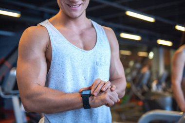 Çekici genç kaslı adam onun etkinlik izleyicisi'ni seyir ve spor salonunda bir koşu bandı üzerinde çalıştırırken gülümseyen