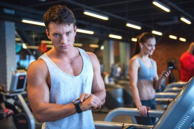 Çekici genç kaslı adam onun etkinlik izleyicisi'ni seyir ve spor salonunda bir koşu bandı üzerinde çalıştırırken gülümseyen