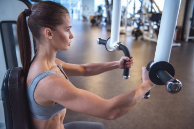 Güzel genç kadın fitness istasyonda demir spor salonunda pompa çalışıyor