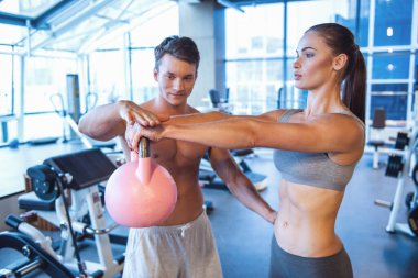 Çekici genç kadın kettlebell spor salonunda çalıştığını, yakışıklı kaslı eğitmen ona yardım ediyor
