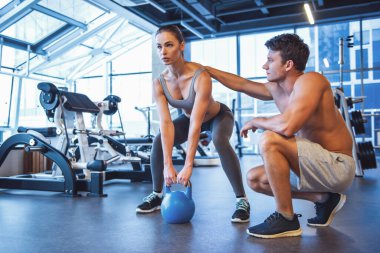 Çekici genç kadın kettlebell spor salonunda çalıştığını, yakışıklı kaslı eğitmen ona yardım ediyor
