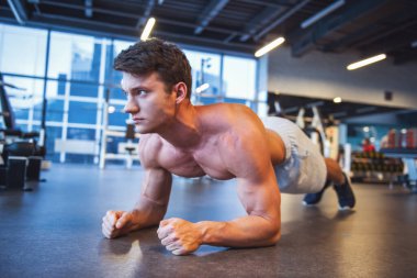 Çekici genç kaslı adam spor salonunda dışarı çalışırken tahta egzersiz yapıyor