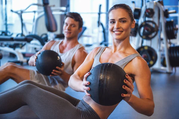 Attractive young muscular man and woman are working out with balls in gym