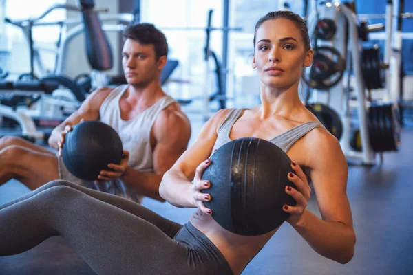 Attractive young muscular man and woman are working out with balls in gym