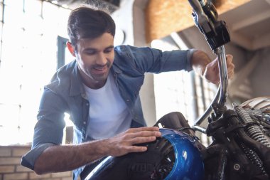 Çekici bir adam bir motosiklet tamircisi incelenirken gülümsüyor