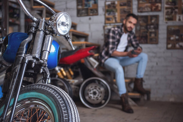 Modern motorcycle repair shop. Motorbike in the foreground, man is sitting in the background