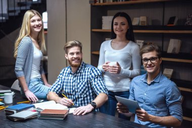 Genç akıllı insanlar kameraya bakıyor ve modern kütüphanede okurken gülümseyen