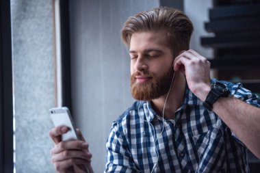 Kulaklık yakışıklı genç adam bir smartphone kullanarak kapalı gözler ile müzik keyfi