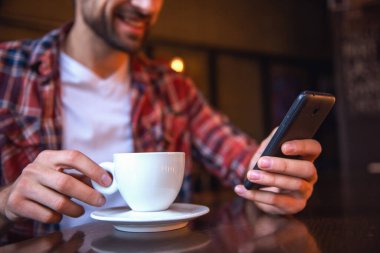 Yakışıklı bir smartphone kullanarak, kahve içme ve kafede otururken gülümseyen