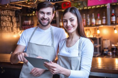 Güzel genç garson kameraya bakarak ve bar yakınındaki dururken gülümseyen bir dijital tablet kullanıyorsanız Cafe counter