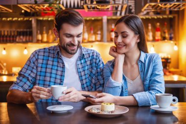 Mutlu genç çift bir smartphone kullanarak ve kafede otururken gülümseyen