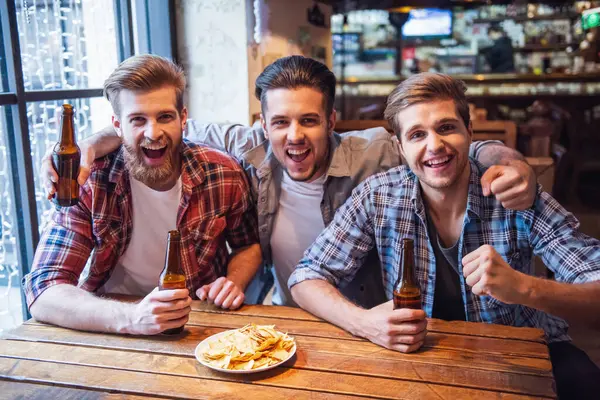 stock image Handsome friends are drinking beer, looking at camera and smiling while resting at the pub