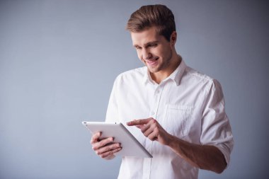 Yakışıklı işadamı dijital tablet kullanma ve gri arka plan üzerinde gülümseyen