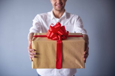 Bir büyük hediye kutusu gri arka plan üzerinde onun çift için tutarken gülümseyen yakışıklı Romantik adam Resim kırpılmış