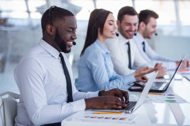 Çekici iş adamları takım elbise ve kulaklık dizüstü bilgisayarlar Office ile çalışırken gülüyorsun