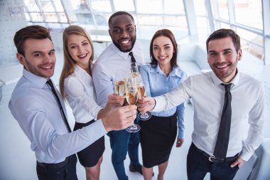 Başarılı iş adamları ofiste kutlama yaparken şampanya bardaklarını tokuşturup gülümsüyorlar.