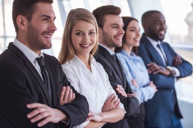 Güzel iş takım resmi elbiseli Office çapraz silah ile üst üste duran gülümseyerek. Kız kameraya bakıyor