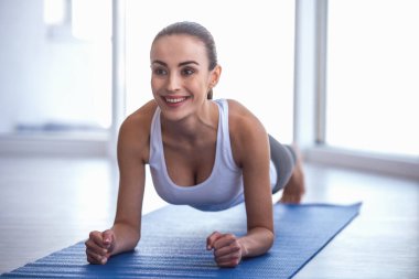 Spor giyim güzel kızı tahta egzersiz yoga mat yaparken gülümsüyor