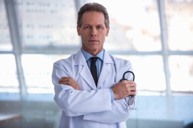 Yakışıklı olgun doktor stetoskop bir holding ve katlanmış silah ile dururken kamera bakıyor