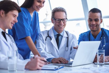 Başarılı tıp doktorları bir dizüstü bilgisayar kullanarak ve bir tartışma yaparken gülümseyen