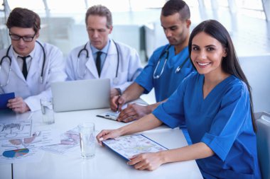 Başarılı tıp doktorları bir dizüstü bilgisayar kullanarak ve belgeleri konferans sırasında tartışıyor. Güzel kadın doktor kameraya bakarak ve gülümseyen