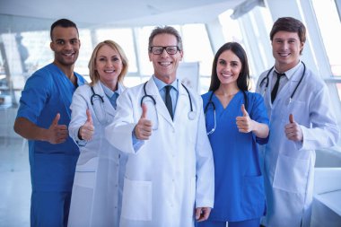 Tıp doktorları başarılı ekibi vardır gösteren başparmak, kameraya bakarak ve hastanede dururken gülümseyen