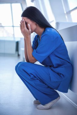 Mavi önlük içinde güzel doktor hastane koridorda onu kıç üzerinde otururken yüzünü kaplayan