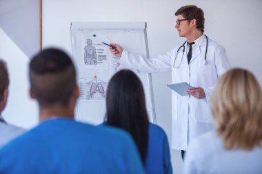 Yakışıklı tıp doktoru bir beyaz tahta ve düzenleri kullanarak meslektaşları için ders veriyor