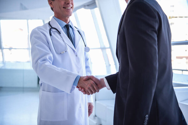 Cropped image of handsome mature doctor and young businessman shaking hands while standing in the hospital hall