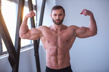 Çıplak gövde ile yakışıklı kaslı adam kameraya bakıyor ve kasları dururken spor salonunda gösterilen