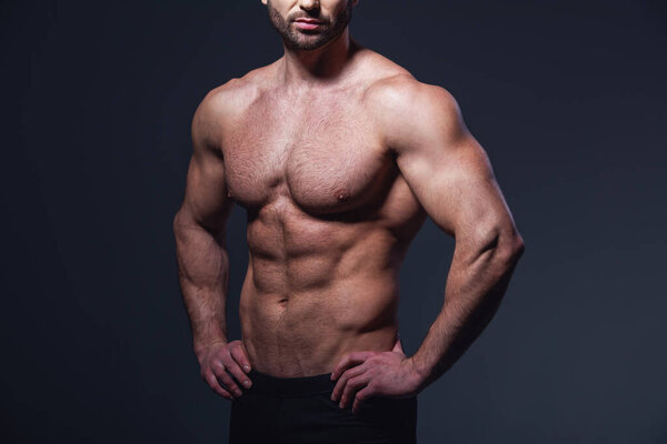 Cropped image of handsome muscular man with bare torso showing muscles, on dark background