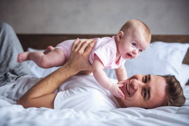 Yakışıklı genç Baba onun şirin bebek ile oynarken, kameraya bakıyor ve gülümsüyor