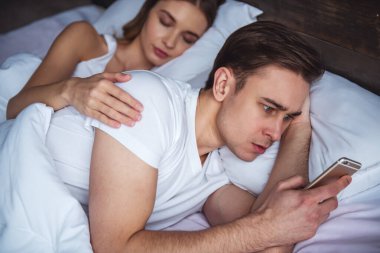 Genç çift having a problem. Adam kız arkadaşı uyku ve onu sarılma bir smartphone kullanarak sohbet