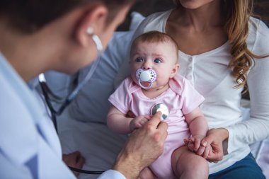 Doktor bebeğin akciğerleri dinlerken güzel genç anne şirin bebeği tutuyor