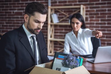 Kovulmak. Takım elbiseli yakışıklı işadamı eşyaları ile arka planda kadın uzağa işaret bir kutu tutuyor