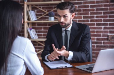 Takım elbiseli yakışıklı işveren ofisinde otururken bir iş görüşmesi yürütüyor