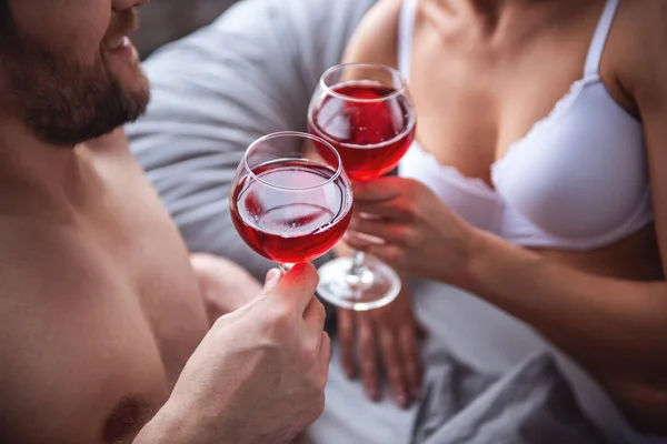 Beautiful couple is drinking wine, talking and smiling while spending time together in bed at home