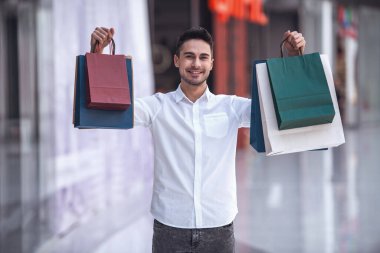 Yakışıklı olan alışveriş torbaları ile kameraya bakarak ve çarşıda alışveriş yaparken gülümseyen