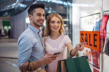 Güzel çift alışveriş torbaları ile bir smartphone kullanarak ve çarşıda alışveriş yaparken gülümseyen