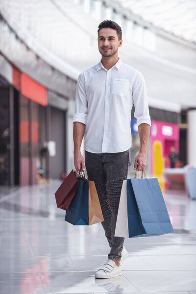Full length portrait of handsome guy with shopping bags smiling while doing shopping in the mall