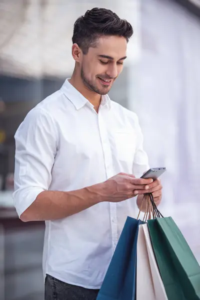 Handsome Guy Shopping Bags Using Mobile Phone Smiling While Doing — Stock Photo, Image
