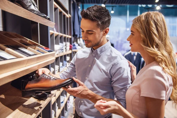 Beautiful couple is choosing classic shoes and smiling while doing shopping in the male store