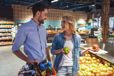 Güzel çift elma seçme ve süpermarkette alışveriş yaparken gülümseyen