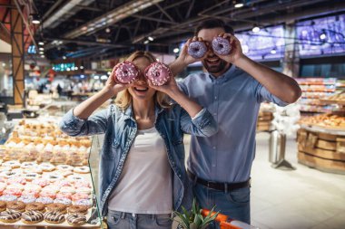 Güzel çift donuts tutarak ve süpermarkette alışveriş yaparken gülümseyen