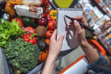 Süpermarkette alışveriş yaparken malların listesini tutan güzel genç kadın Resim kırpılmış