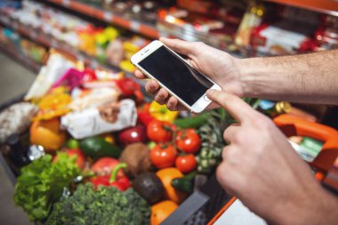 Süpermarkette alışveriş yaparken bir cep telefonu kullanan adam Resim kırpılmış