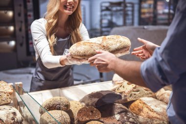 Süpermarkette. Bir ekmek müşteriye sunan ve gülümseyen güzel genç kadın işçinin Resim kırpılmış