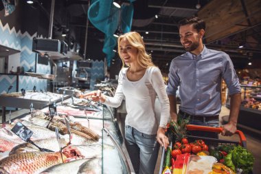 Güzel genç çift balık seçme ve süpermarkette alışveriş yaparken gülümseyen