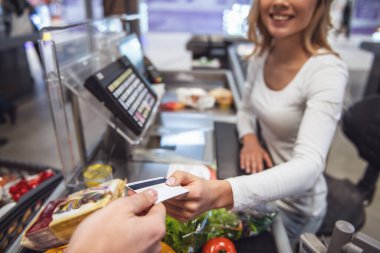Güzel genç kasiyer kredi kartı tutan ve markette çalışırken gülümseyen